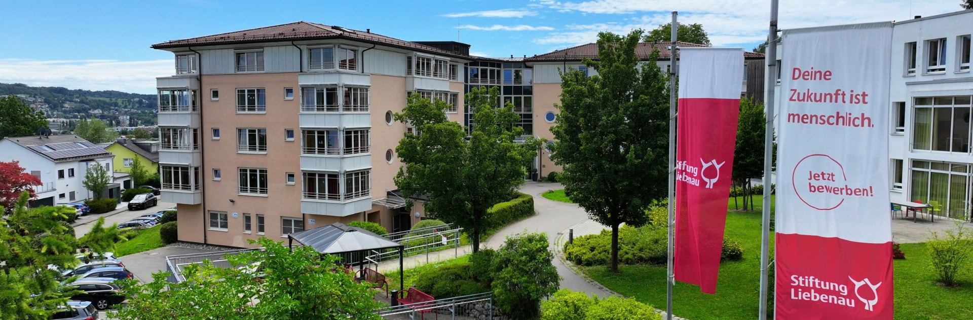 Haus Meinrad – Außenansicht mit Fahnen der Stiftung Liebenau